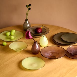 トゥモローランドがガラス工房とコラボレーションした黄色や紫の花瓶やプレート、ボウルを並べたテーブル