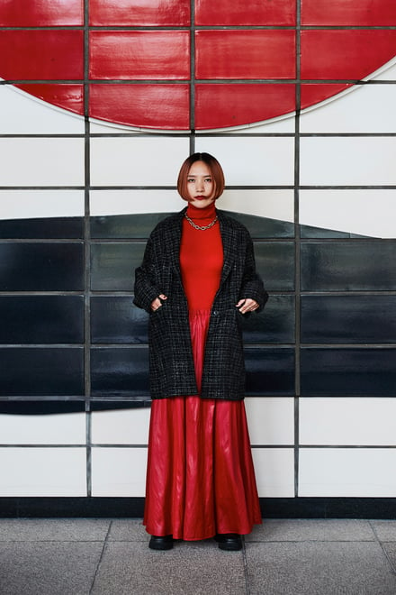 新ブランド「エニカ」のヴィジュアルで赤いワンピースとチェックジャケットを着用したモデル