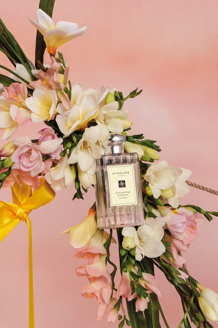 白やピンクの花々と香水のボトルの画像