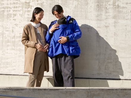 ザ・ノース・フェイスの青いマタニティ用ジャケットを着用した男性とその横に立つ女性