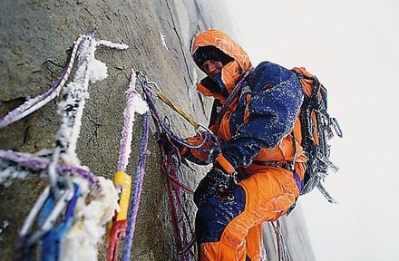 オレンジのウェアを着用して登山をする男性