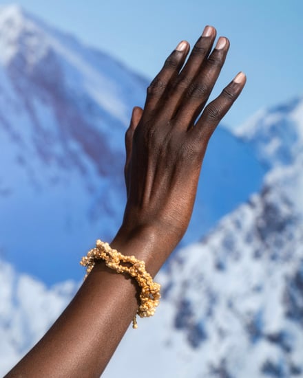 雪山を背景にゴールドのバングルを着用した人の手