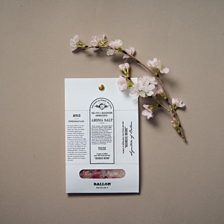 中央にペーパーバッグに入ったバスソルトとその上方に花が咲いた桜の切り枝を映した写真