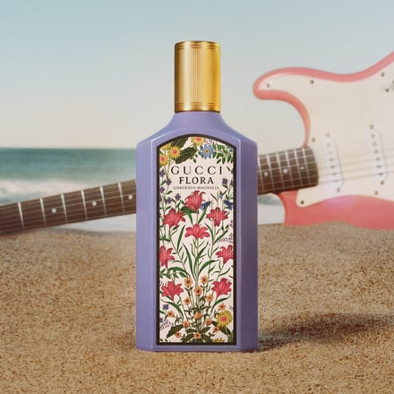 砂浜に置かれたパステルパープルの香水ボトルとピンクのギター