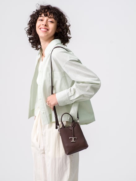 白色の背景、鞄の紐を持って笑う女性
