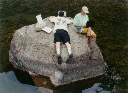 大きな岩の上でPC作業をする男性2人