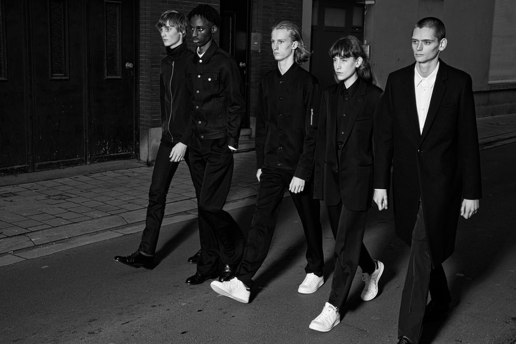 黒のジャケットとスラックスを身につけた6人の男性が歩いている様子