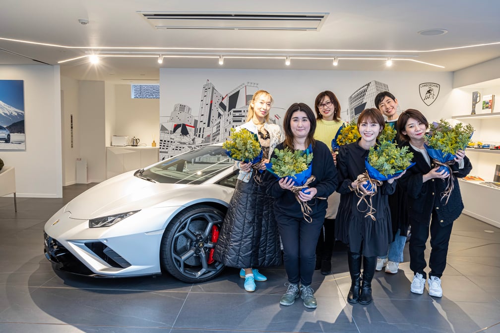シルバーのランボルギーニの前で花束を抱える女性たち