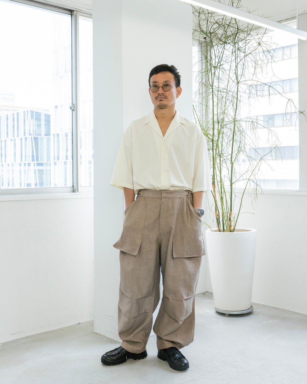 白い開襟シャツにリネンのワークパンツを合わせた男性モデル