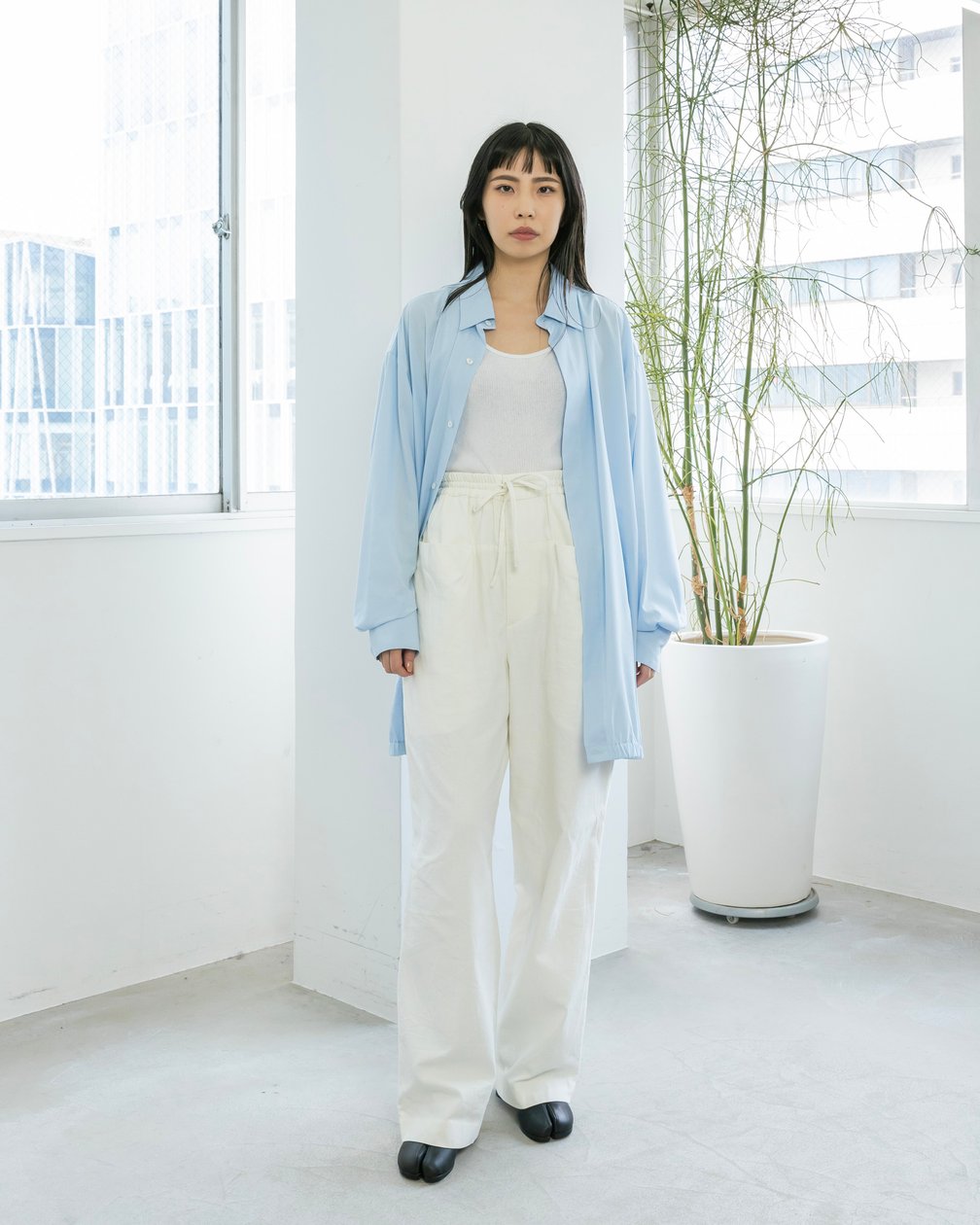 青いシャツにホワイトのワイドパンツを着用した女性