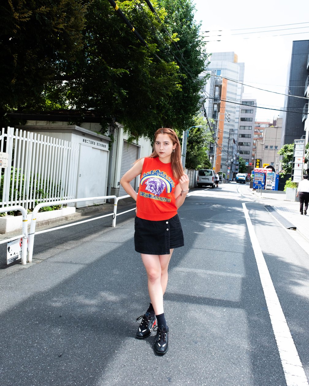 オレンジのニットベストにブラックのスカートを着用した女性モデル