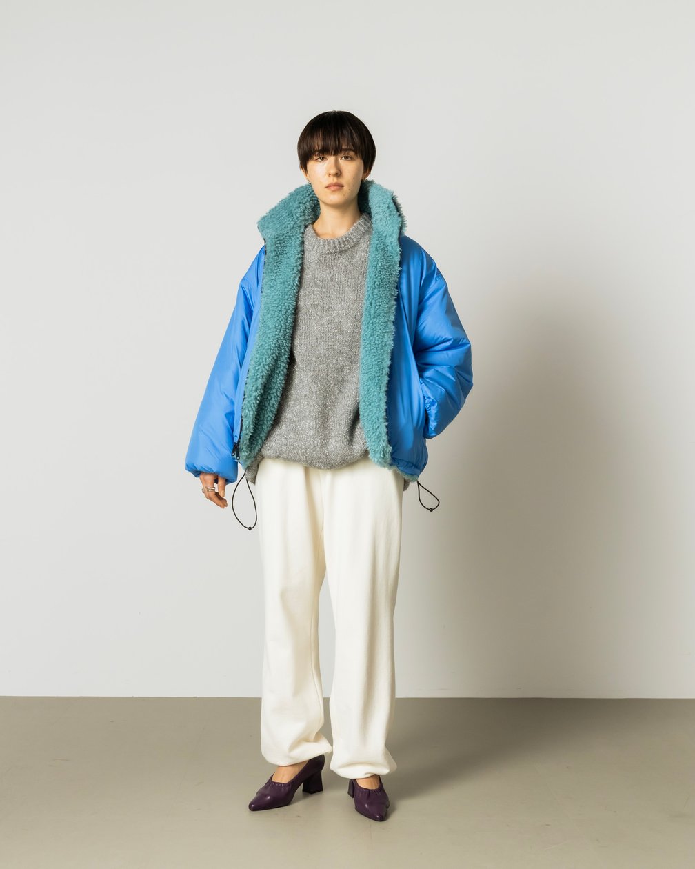 シルバーのラメニットにブルーのブルゾンを合わせた女性モデル