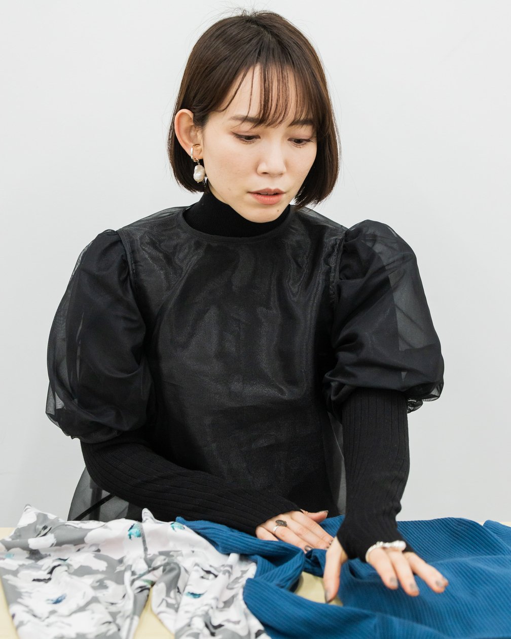 ブルーのトップスを触っている黒いワンピースを着たボブの女性