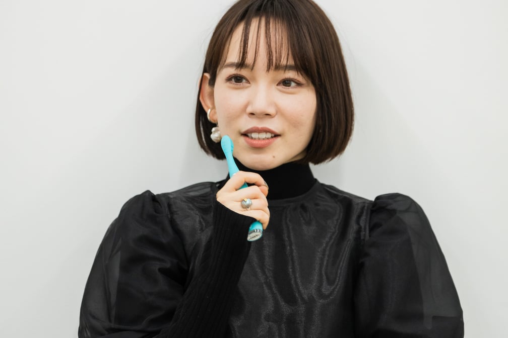 グリーンの電動歯ブラシを手に持つ女性