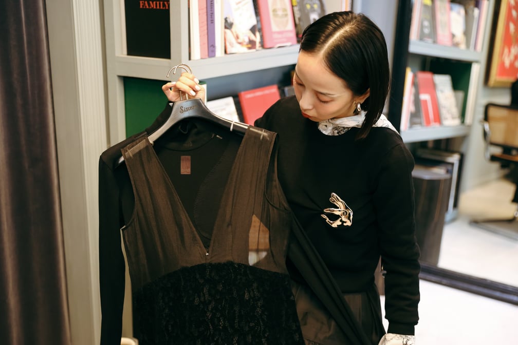 黒い服を着て手にハンガーを持って椅子に座る長尾悠美