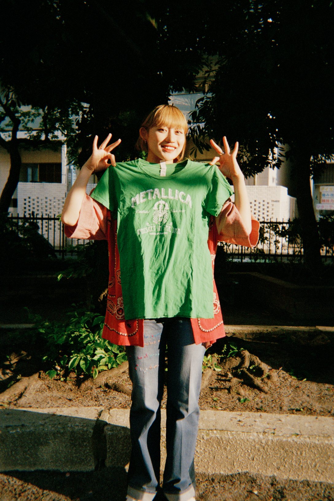 グリーンのメタリカのTシャツを胸元で掲げる佐々木莉佳子