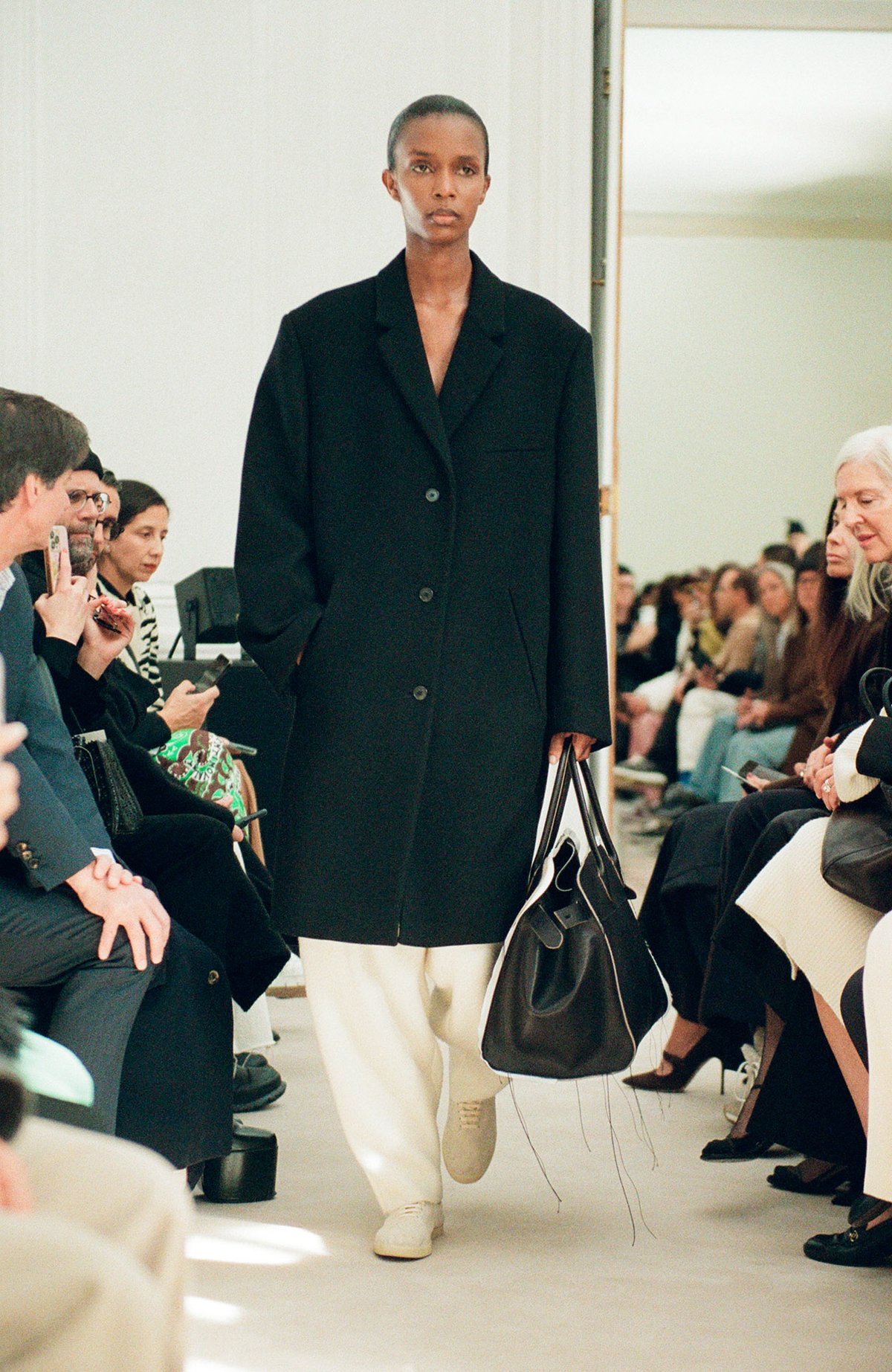 黒いコートと白いパンツを着てランウェイを歩く黒人女性モデル