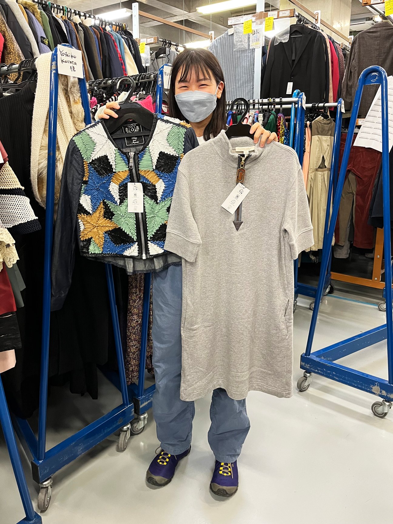 グレーのワンピースとアウターのアイテムを手に持つ女性