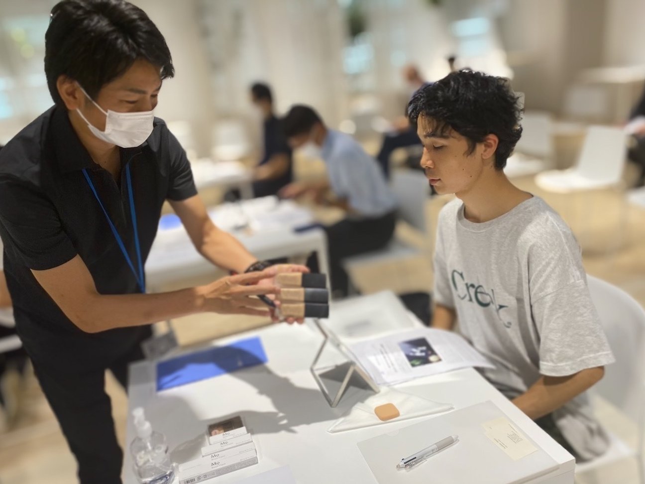 ファンデーションを手に持つ男性と、座っている男性
