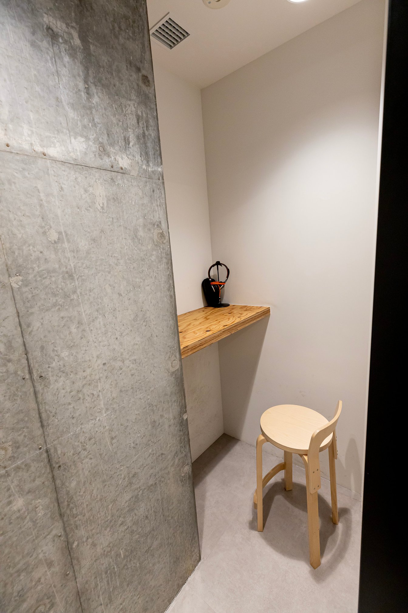 コンクリート壁奥に木材のテーブルと椅子が置かれたフォンブース