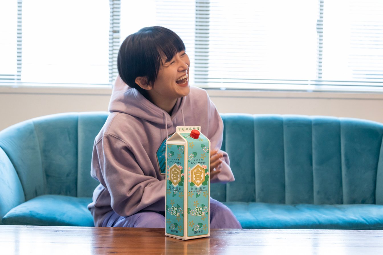 ソファに座るサーヤと水色のパッケージのキンミヤ焼酎
