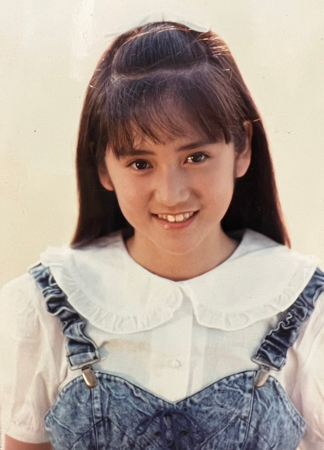 白いブラウスにデニムのオーバーオールを着てカメラ目線で笑顔の少女