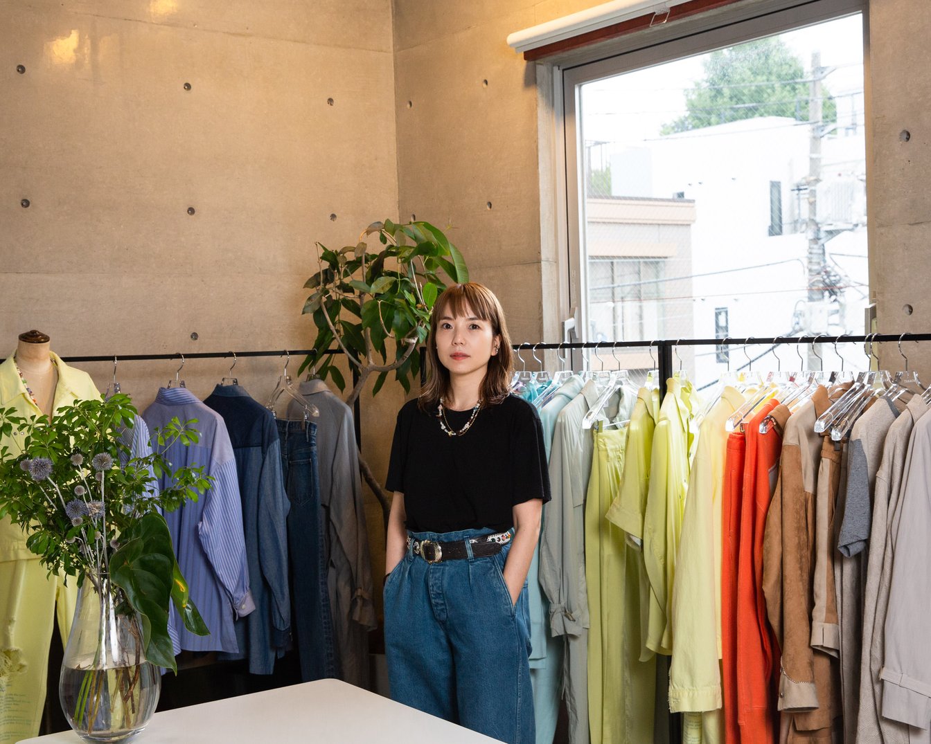 服が並ぶアトリエにたたずむ女性デザイナー