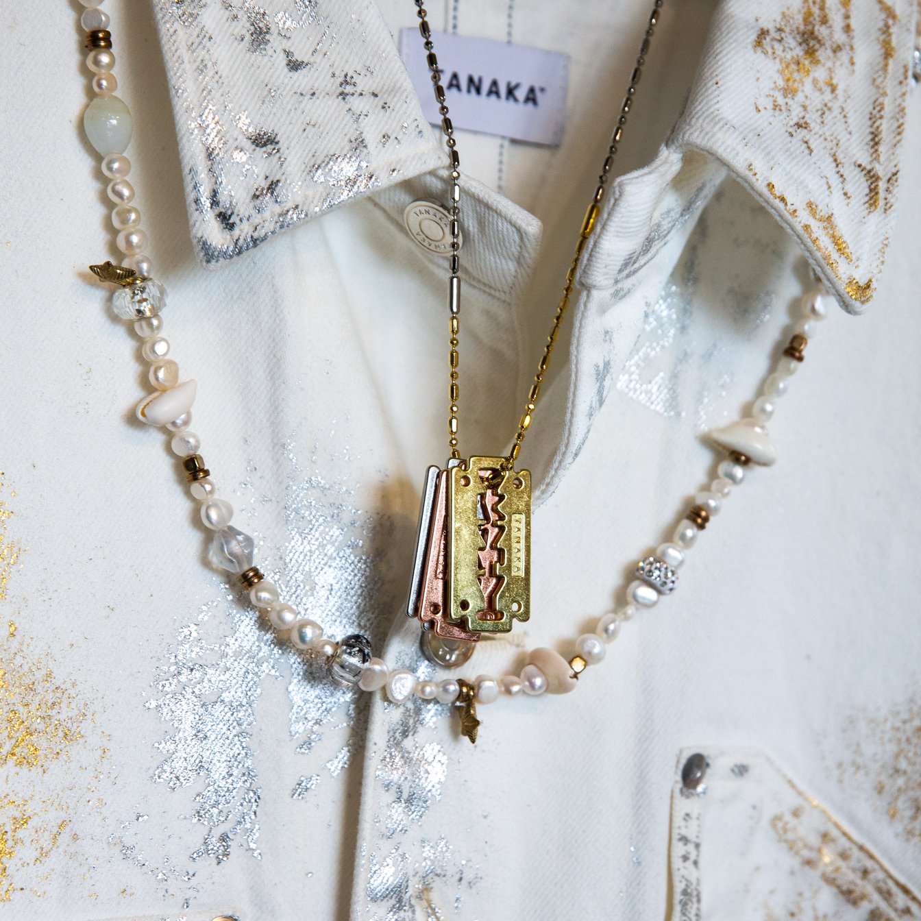 白のデニムジャケットにゴールドのネックレスとビーズアクセサリーを合わせた様子