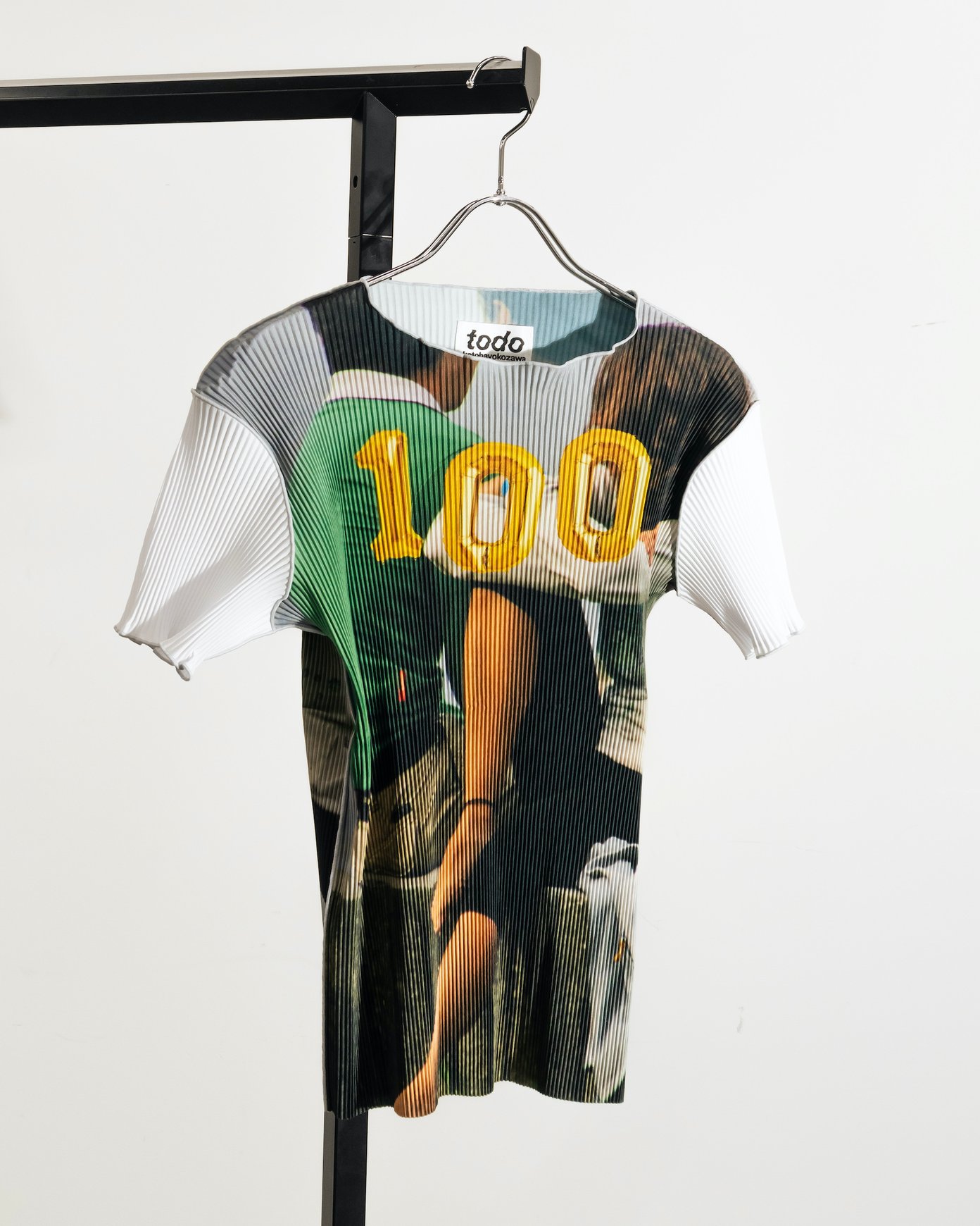 「100」のグラフィックをあしらったコトハヨコザワのプリーツトップス