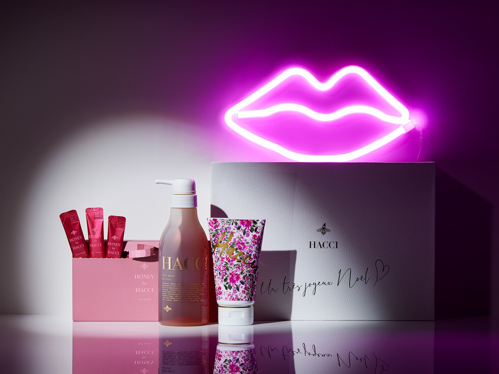 花柄のボディクリーム、透明容器に入ったボディソープ、ピンクの洗顔料とリップ型のネオンサイン