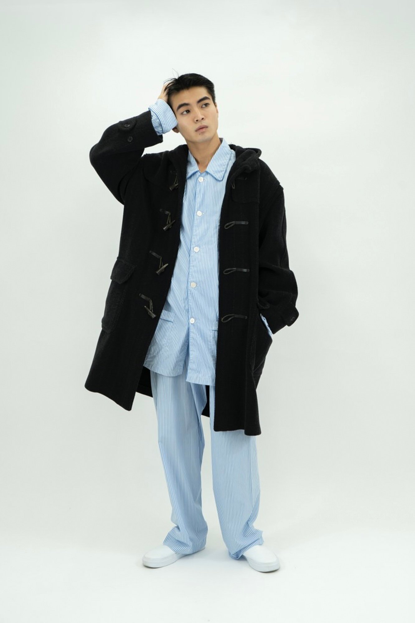 青のシャツとスラックスのセットアップの黒のコートを羽織った男性