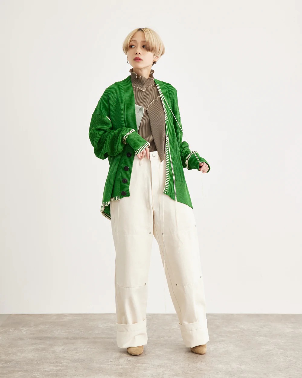 グレーのプリーツトップスにグリーンのカーディガンを着用した女性モデル