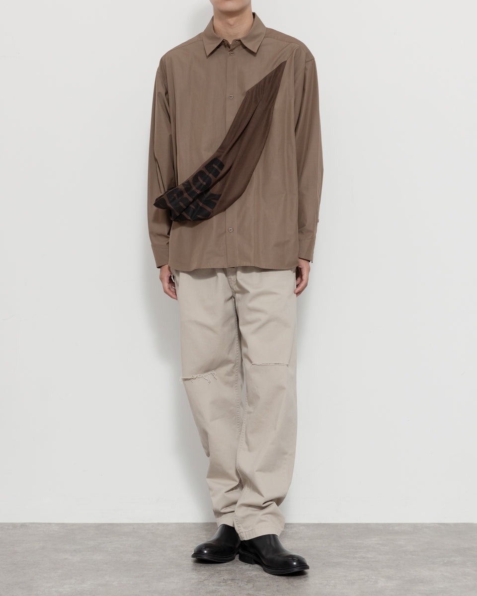 ブラウンのシャツ、ダメージの入ったチノパンツを着用している男性モデル