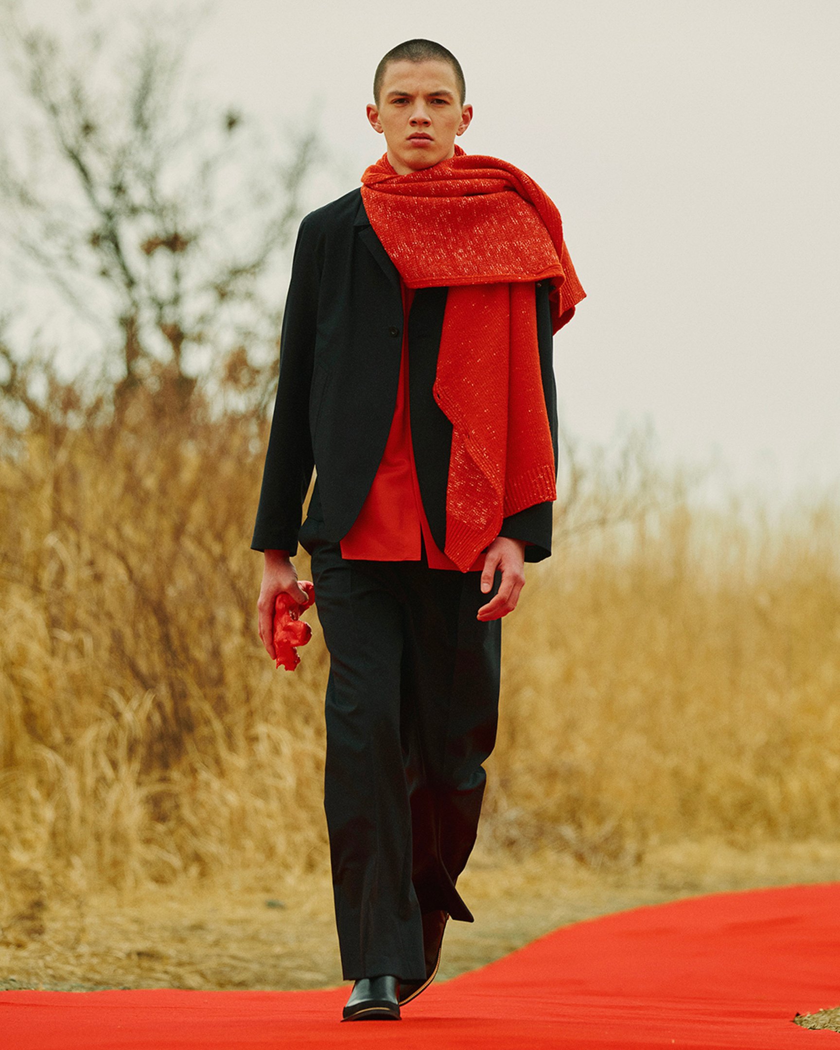 黒のセットアップに朱色のマフラーを合わせた男性モデル