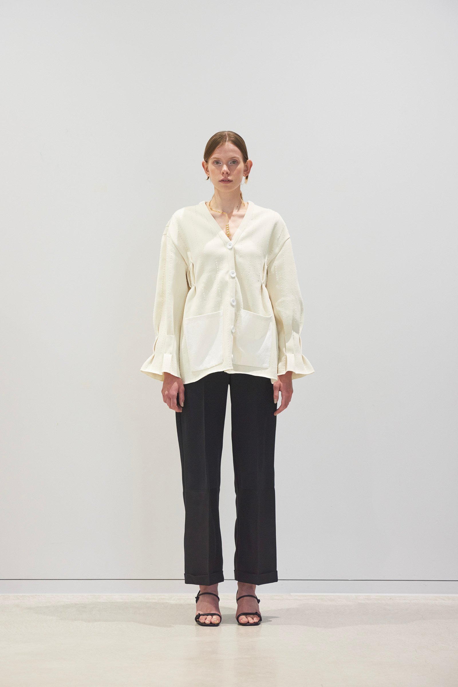 白いカーディガンにブラックのパンツを合わせた女性モデル