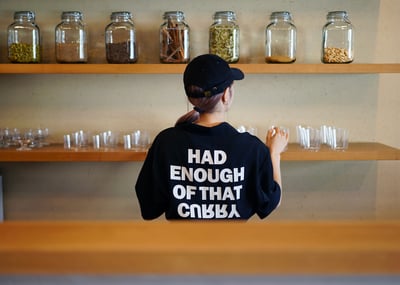 黒いTシャツを着用し壁の棚にグラスを並べる女性の後ろ姿