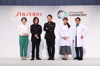 ブランドロゴの書かれた壁の前に並ぶ5人の男女