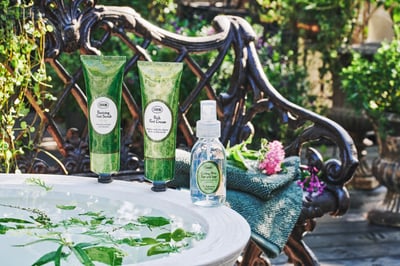 緑の中に置かれたバスタブの縁にあるフットケアアイテム