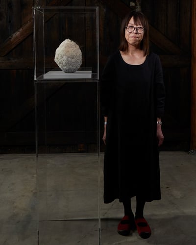 アート作品の横に立つ黒いワンピースを着た女性