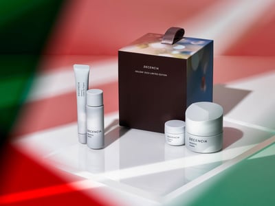 正方形のギフトボックスのそばに並べられた白基調の複数のスキンケア製品のパッケージ