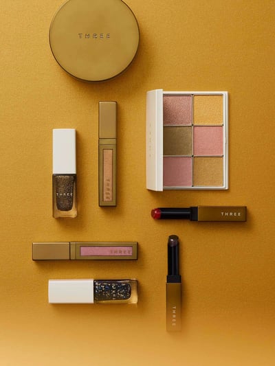 ゴールドの背景にゴールド調のパッケージのコスメがランダムに並べられている