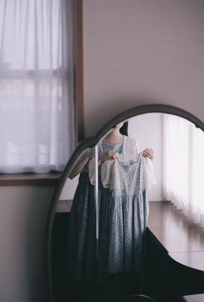 鏡の前で水色のワンピースを手に持つ女性