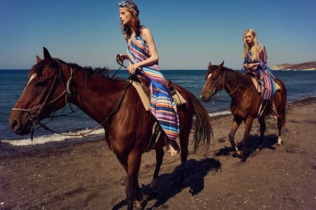 二人の女性がそれぞれ馬に乗り浜辺を歩いている写真