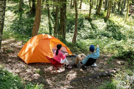 山の中でキャンプをする男女　オレンジ色のテント