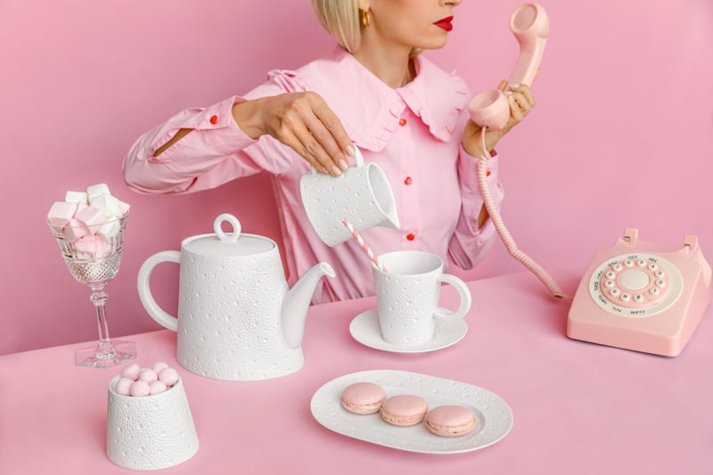 ピンクのブラウスを着用し白い磁器と電話の受話器を持つ女性とピンクのマカロンやマシュマロ