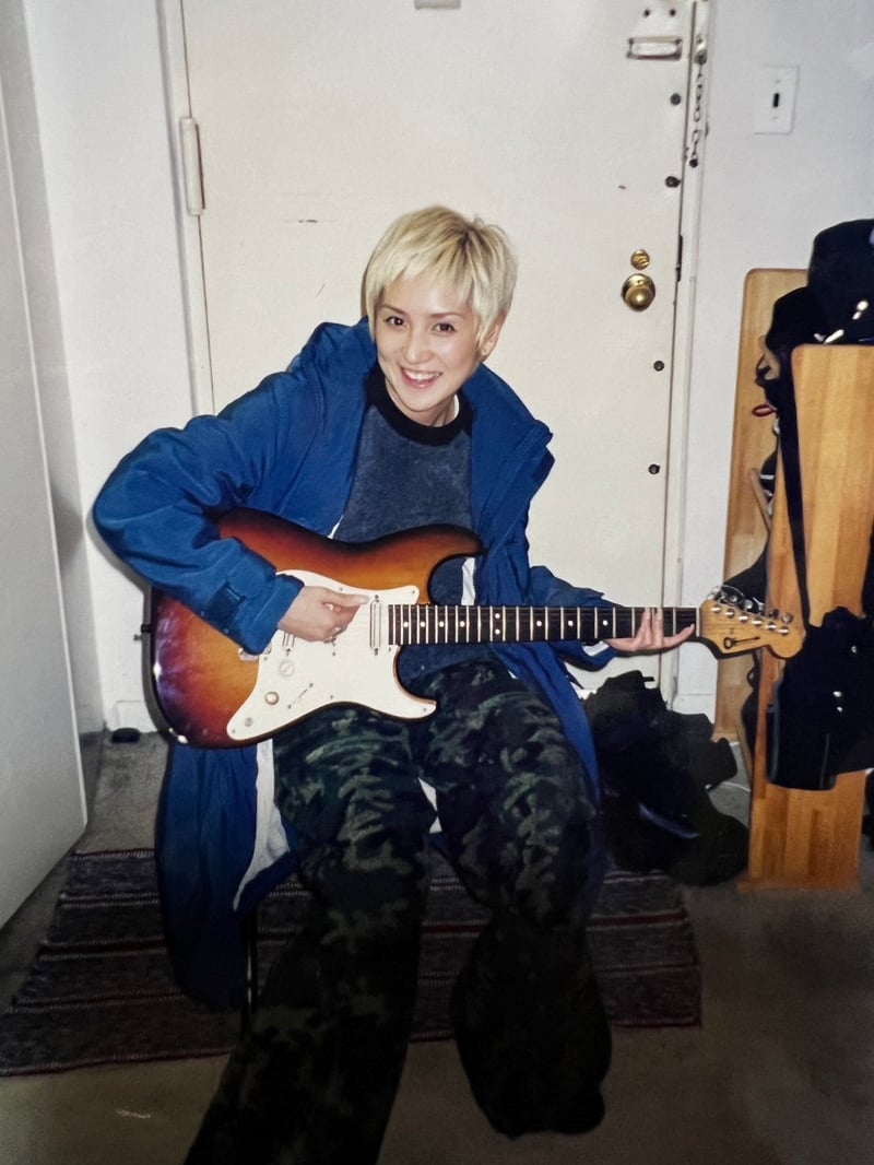 金髪の女性が座りながらギターを持つ写真